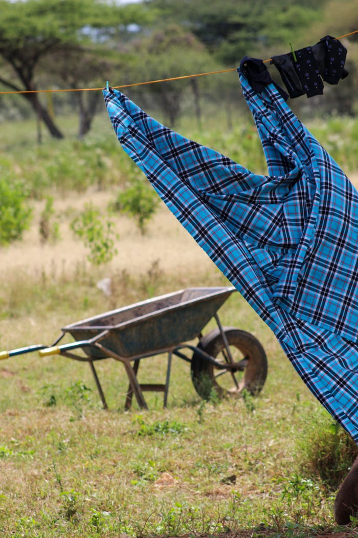 A colorful shirt dries on a clothesline outdoors in rural Kenya with a wheelbarrow in the background.