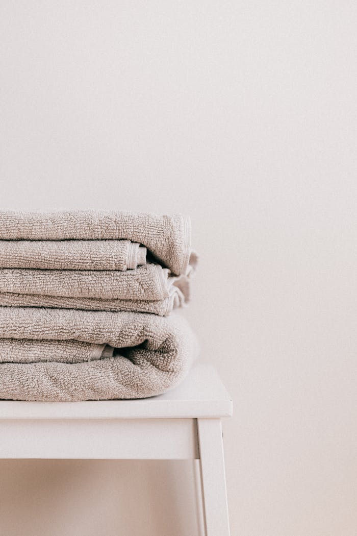 Stack of soft clean fresh gray towels placed on white minimalist stool against beige wall